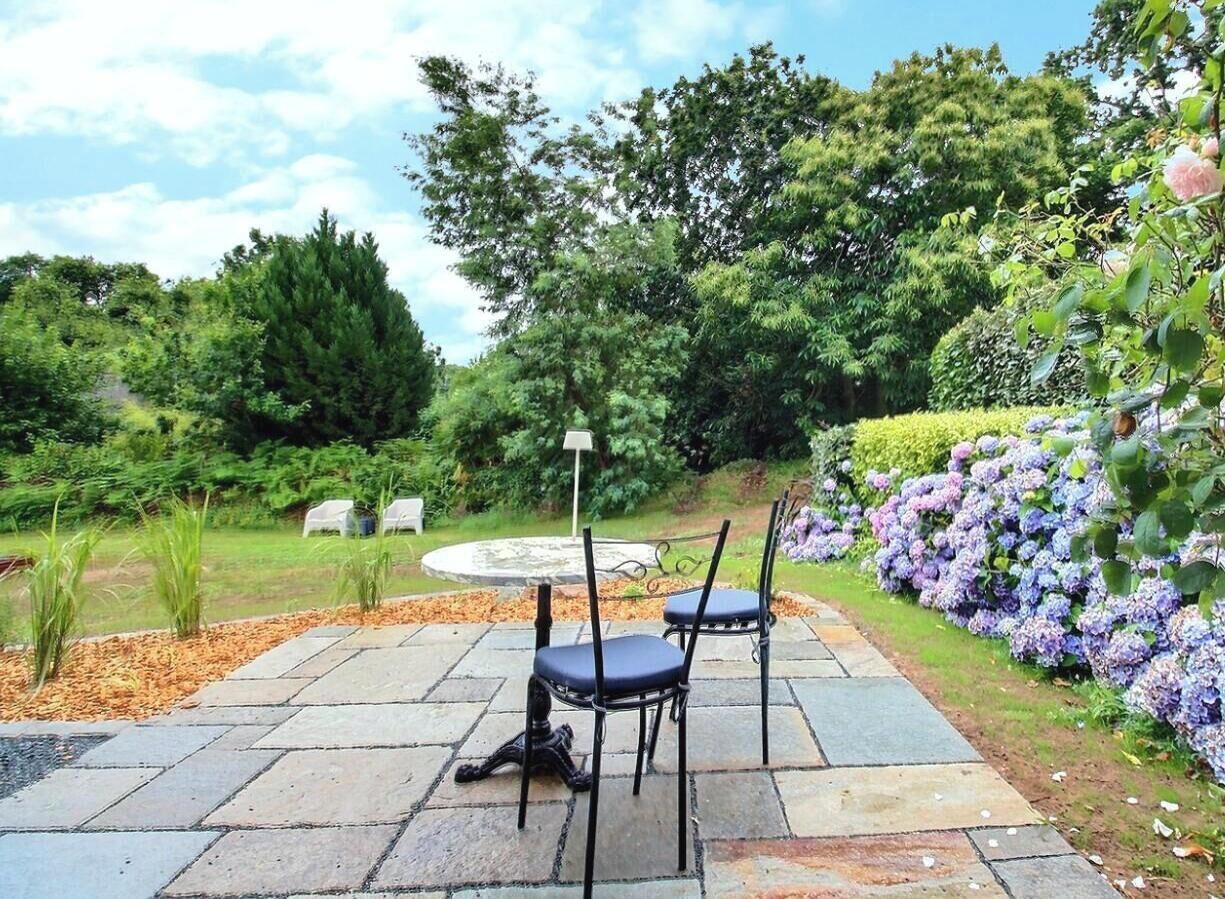 Um pátio externo com piso de pedra, duas cadeiras e uma mesa.