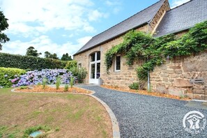 A stone building with a gravel driveway and a flower bed with purple flowers. - KerCoz - PLOUBEZRE - Vacation Rental (PLOUBEZRE)