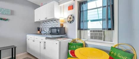 A compact kitchen with white cabinets, a microwave, and a small dining area with a yellow table and chairs.
