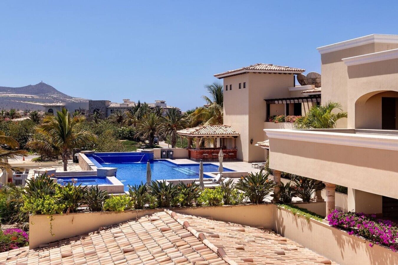 A resort with a swimming pool, palm trees, and a mountain in the background.