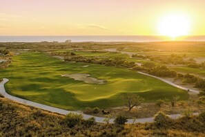 Ein Golfplatz mit gepflegtem Weg, Sandbunkern und einer Fahne auf dem Grün.