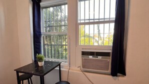 Quarto com duas janelas, uma mesa e duas cadeiras, e um aparelho de ar condicionado.