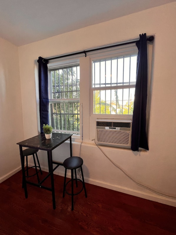 Una habitación con dos ventanas, una mesa con dos sillas y un equipo de aire acondicionado.