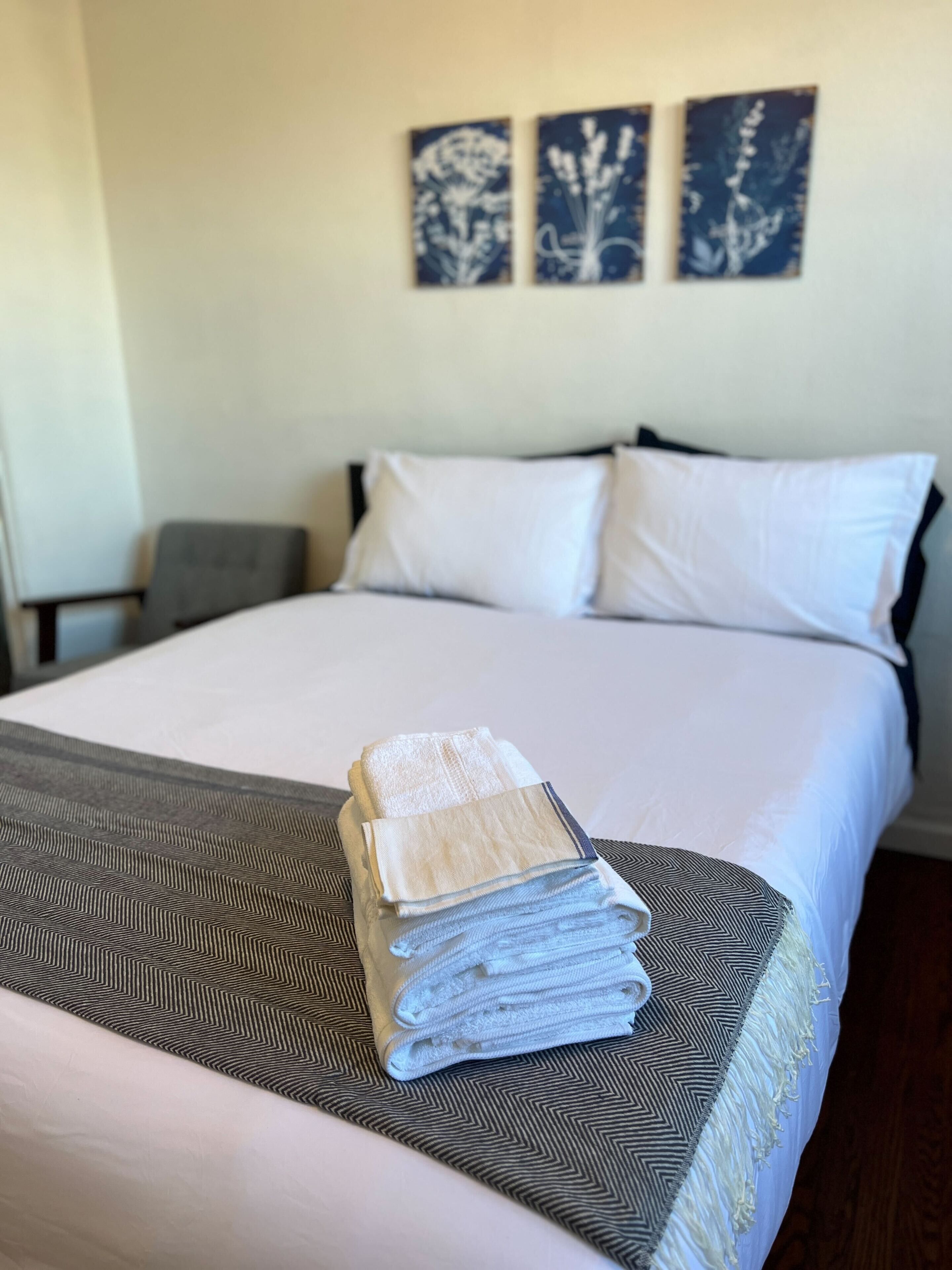 Un lit bien fait, recouvert d’une couvre-lit à motifs, une pile de serviettes pliées et deux œuvres d’art accrochées au mur.