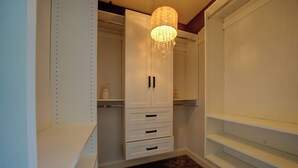 Um closet espaçoso com estantes brancas, um candelabro e piso coberto de carpete.