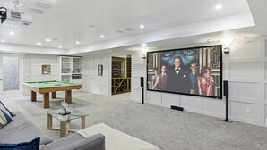Uma sala de entretenimento com mesa de bilhar, área de estar e uma grande TV de tela plana fixada na parede.