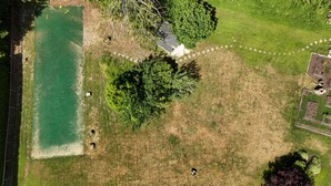 Vista aérea de uma propriedade com área de piscina, jardim cercado e um edifício com telhado característico.