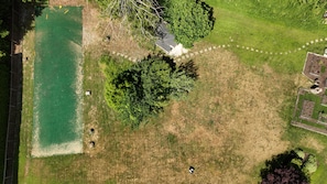 Luchtbeeld van een object met een zwembad, een omheinde tuin en een gebouw met een opvallend dak.