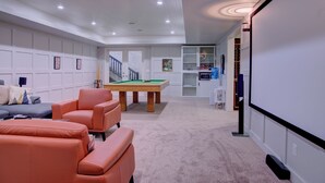 Uma sala de estar moderna com mesa de bilhar, um sofá e tela de projeção.