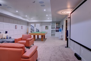 Een moderne woonkamer met een biljart, een bank en een projectiescherm.