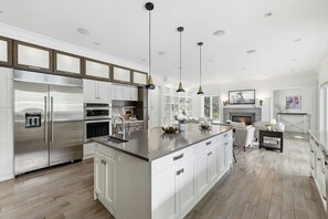 A modern kitchen with stainless steel appliances, a central island, pendant lighting, and a fireplace in the adjacent living area.