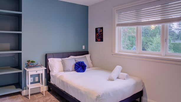 Quarto com cama, mesa de cabeceira, janela com persianas e um quadro na parede.