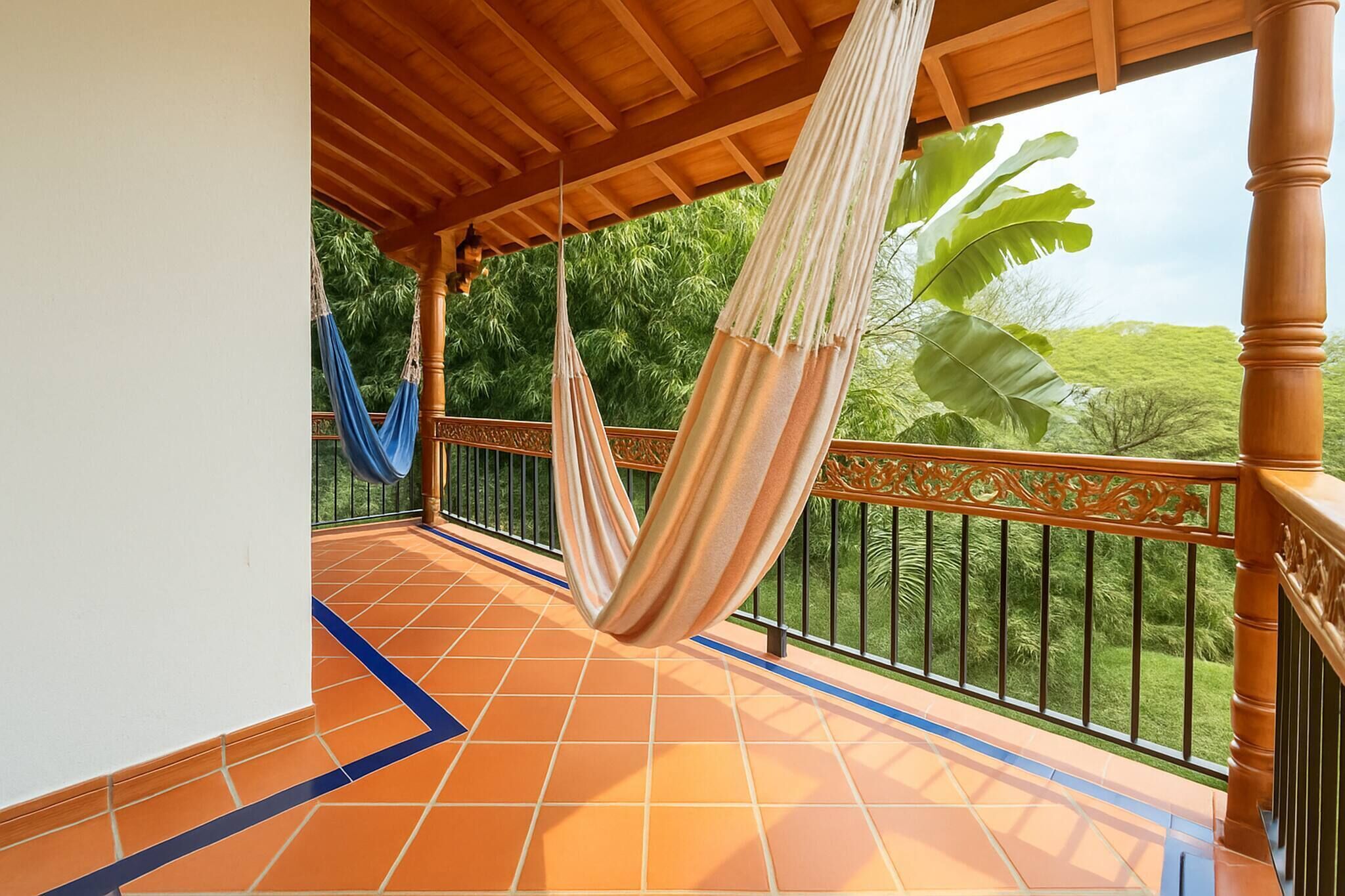 Un balcone coperto con un'amaca, pavimento piastrellato e vista sul verde.