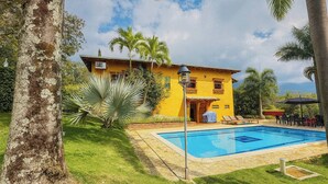 Un edificio amarillo con piscina, rodeado de palmeras y césped.