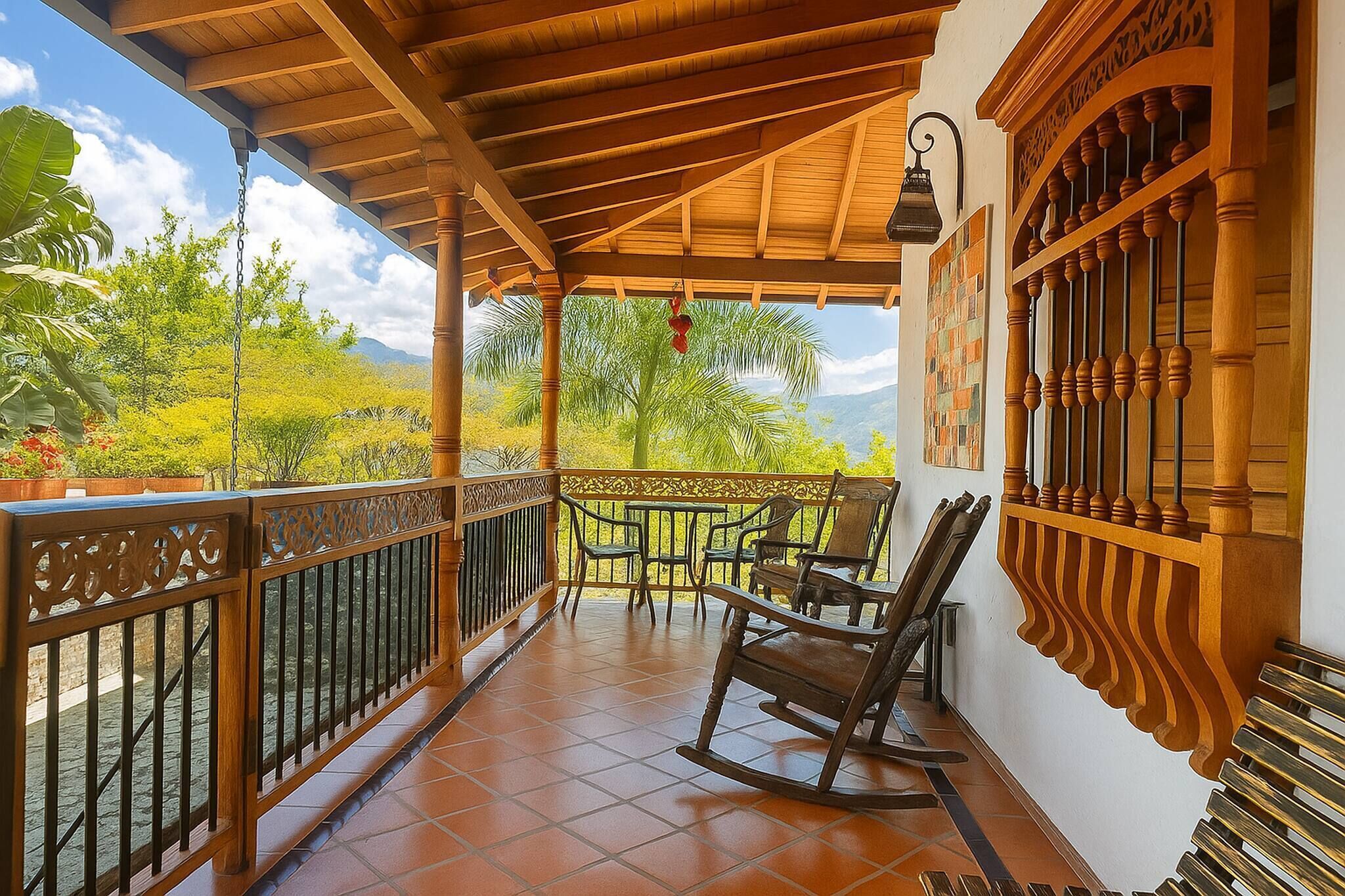 A covered balcony with wooden railings, a rocking chair, and a view of greenery and mountains.