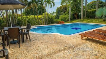 Una piscina con solárium de baldosas, rodeada de palmeras y follaje.