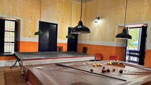 A billiards table with balls and cues, a door, and two hanging lamps in a room with yellow walls.