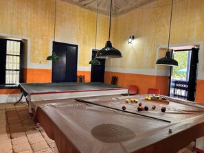 Mesa de billar con bolas y tacos, una puerta y dos lámparas colgantes en una habitación con paredes amarillas.