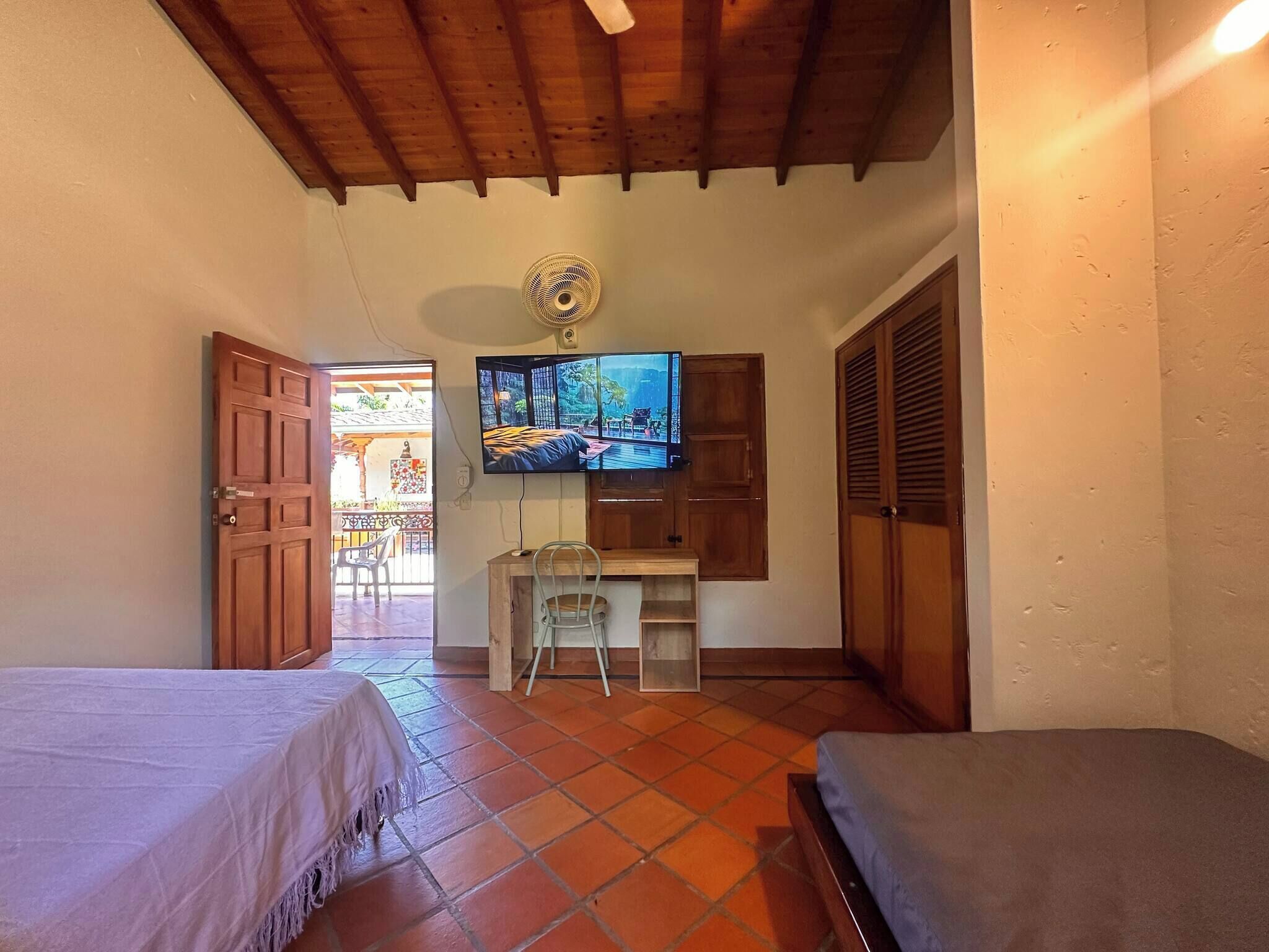 Una habitación con cama, escritorio, silla, televisión y vistas al exterior.