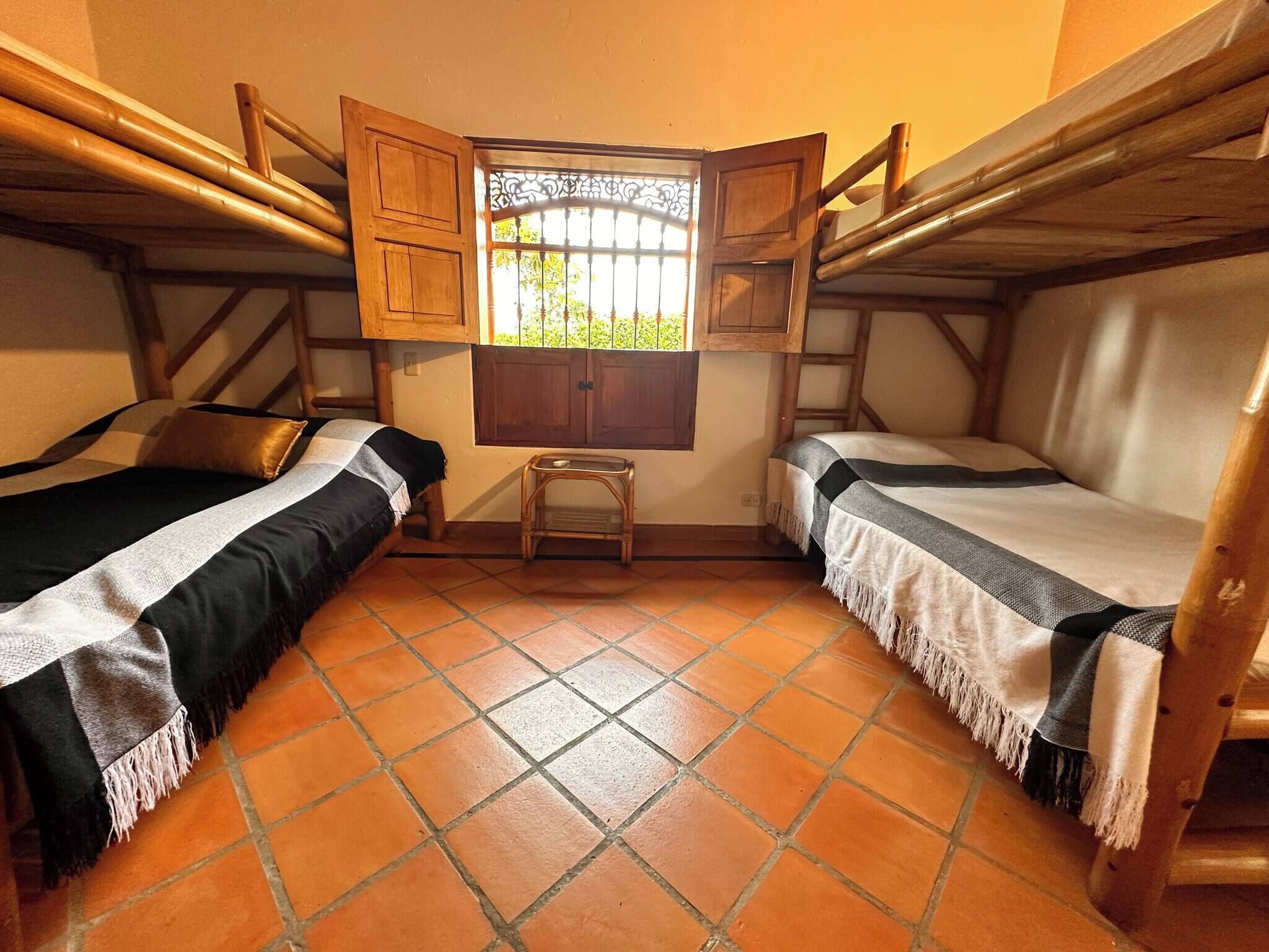Una habitación con dos camas, un taburete pequeño y una ventana con reja de metal.