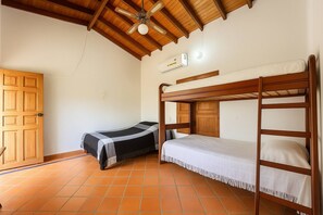 A room with a wooden ceiling, a bunk bed, a single bed, a wardrobe, and a tiled floor.