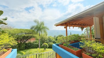 A balcony with a view of a lush garden and distant mountains.