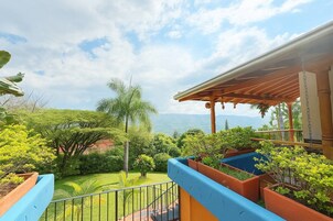 Un balcón con vista a un jardín exuberante y montañas distantes.