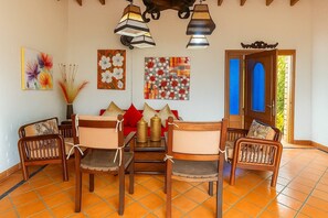 A dining area with wooden chairs and a table, surrounded by artwork and a decorative ceiling light.