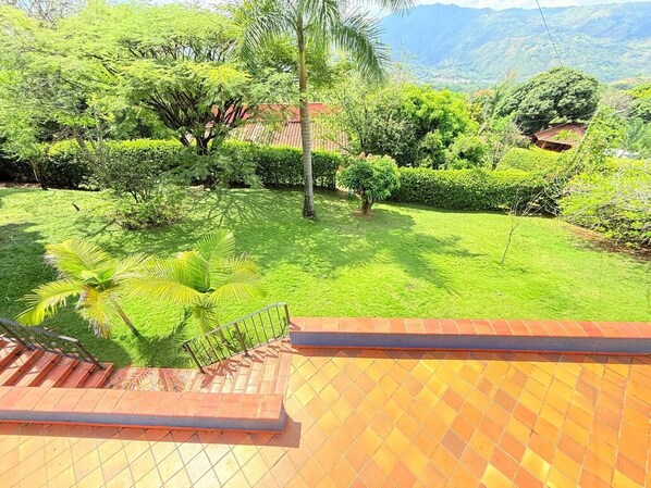 A view of a lush green garden with a variety of trees and shrubs, a clear sky, and a distant mountain range. - Paraíso Las Palmeras With Pool in San Jerónimo (San Jerónimo)