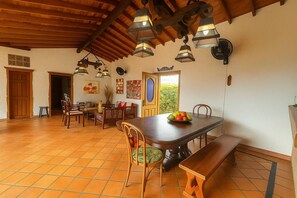 Comedor con mesa de madera, sillas y frutero. Hay luces colgantes y una puerta que da a otra habitación.