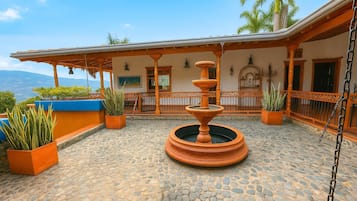 A courtyard with a stone floor, a central fountain, and potted plants.