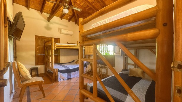 Una habitación con dos literas, techo de madera, televisor y una silla.