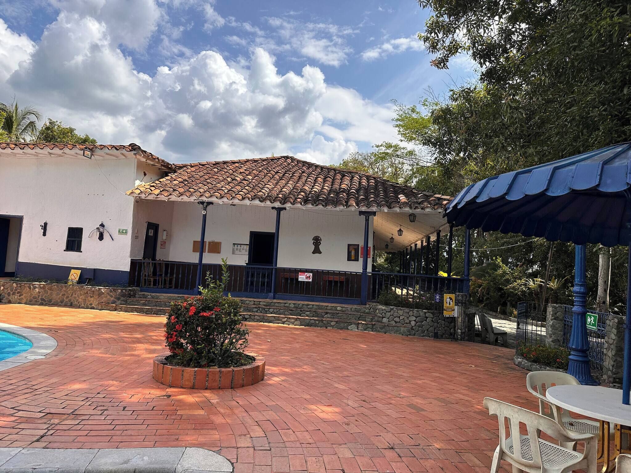 Un edificio con techo de tejas, piscina y patio empedrado con mobiliario exterior.