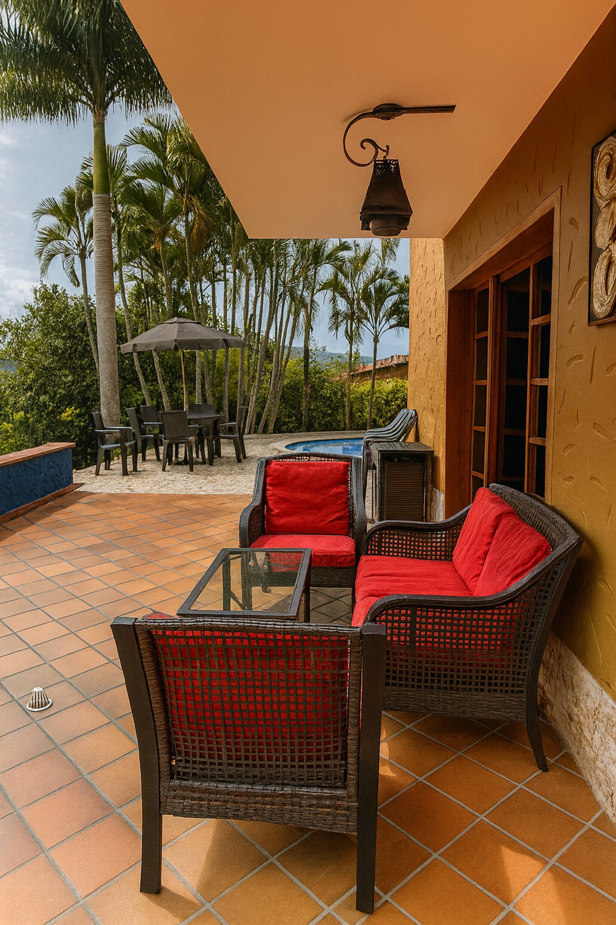 Un patio al aire libre con mobiliario de mimbre, una piscina y vistas a palmeras.