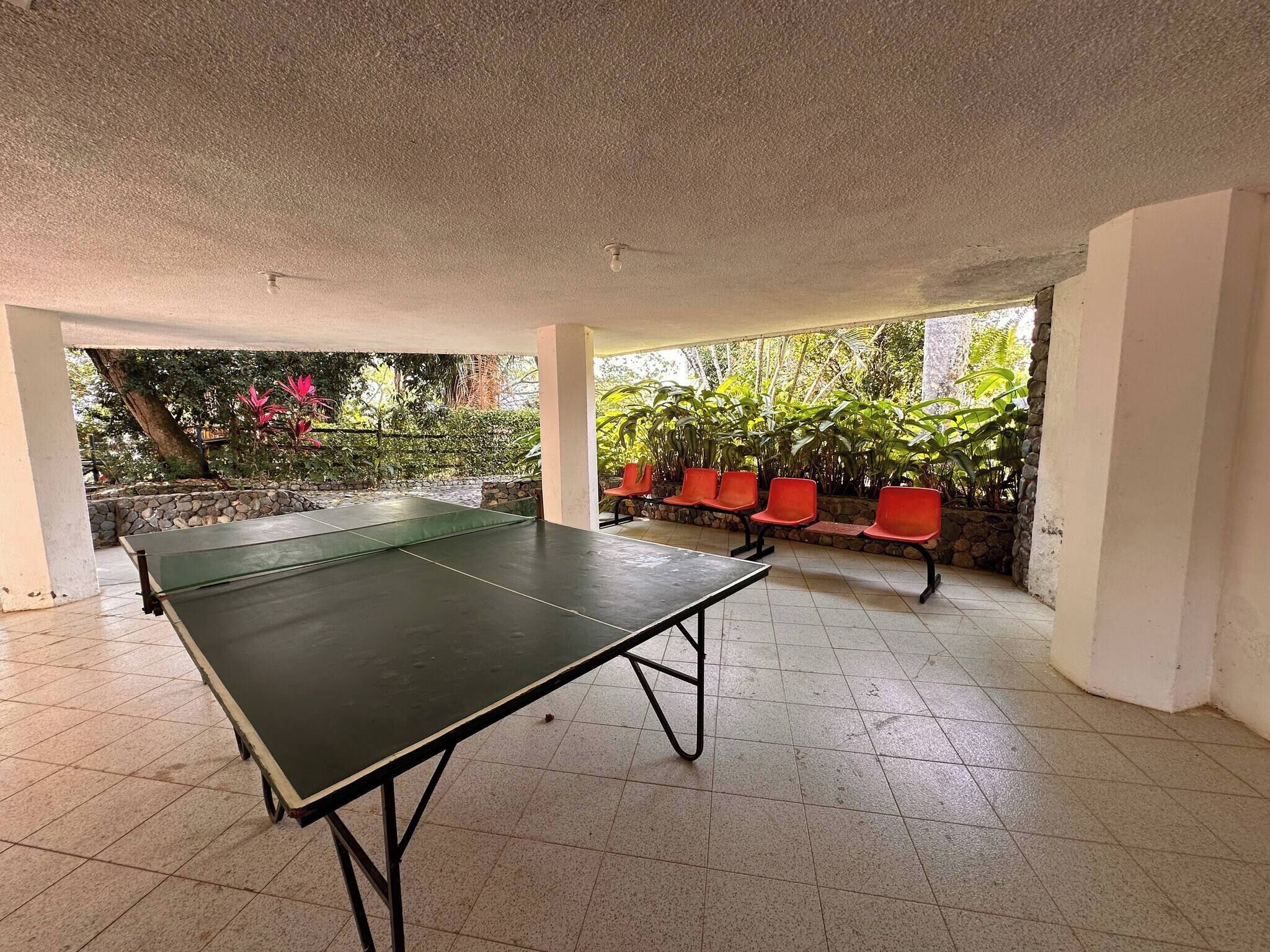 A ping pong table in a covered area with a stone wall and plants.