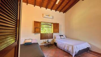A small, cozy room with two beds, a ceiling fan, a window with shutters, and a tiled floor.