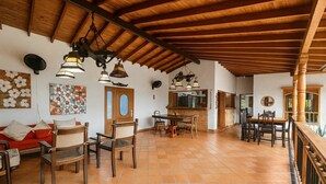Un amplio salón con suelo de baldosas, mobiliario de madera y techo alto con vigas a la vista.