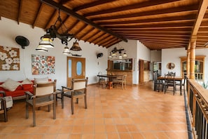 Un amplio salón con suelo de baldosas, mobiliario de madera y techo alto con vigas a la vista.