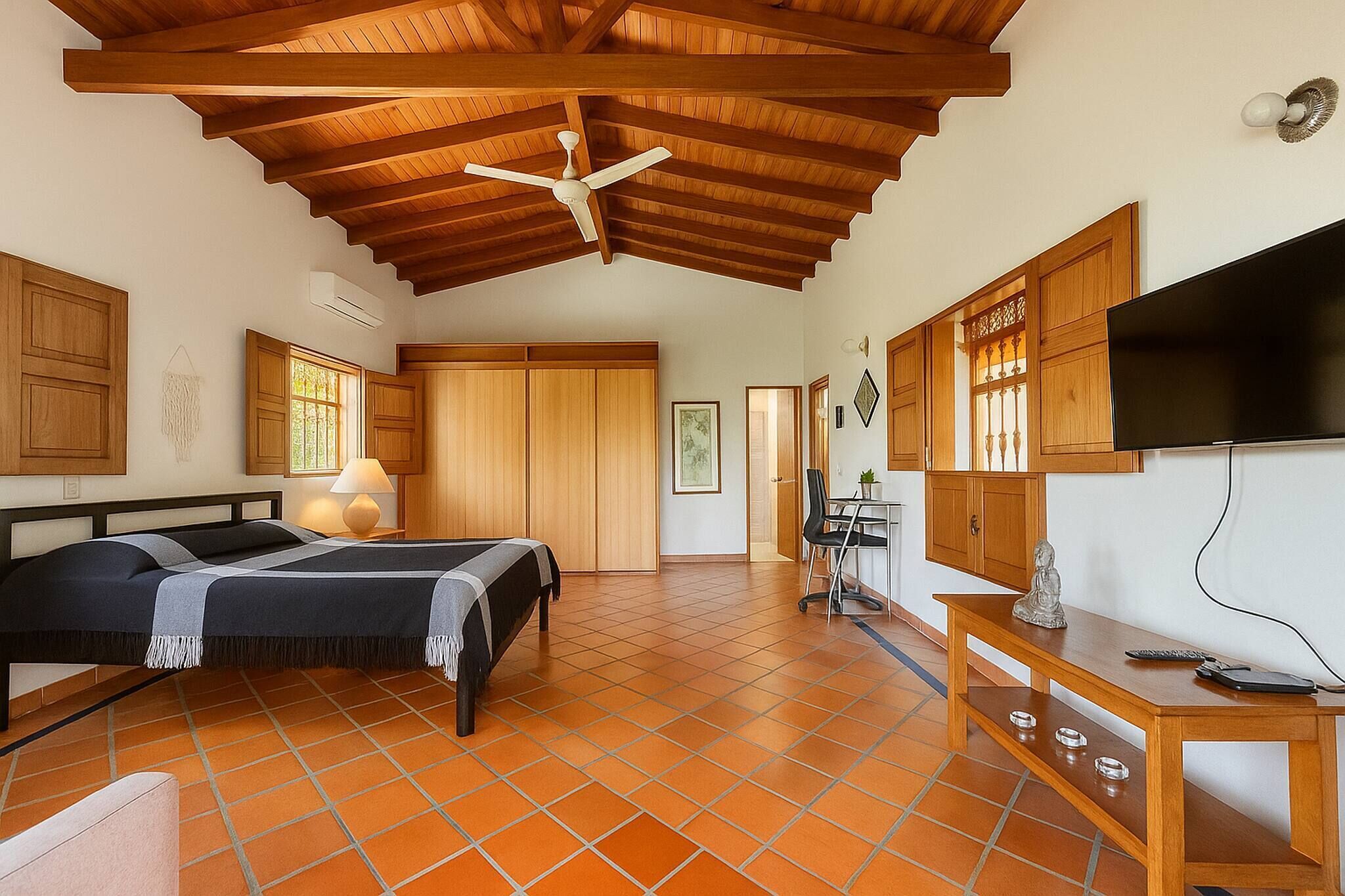 A bedroom with a bed, a desk, a television, and a ceiling fan.