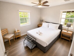 Un dormitorio con cama, una silla, una mesita de noche, una lámpara y un ventilador de techo.