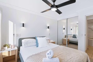 Une chambre d’hôtel moderne équipée d’un lit, de tables de chevet, d’un ventilateur de plafond et d’un grand miroir.
