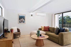 Un salon moderne doté d’un téléviseur à écran plat, d’un canapé, d’une table basse et d’une grande fenêtre donnant sur l’extérieur.