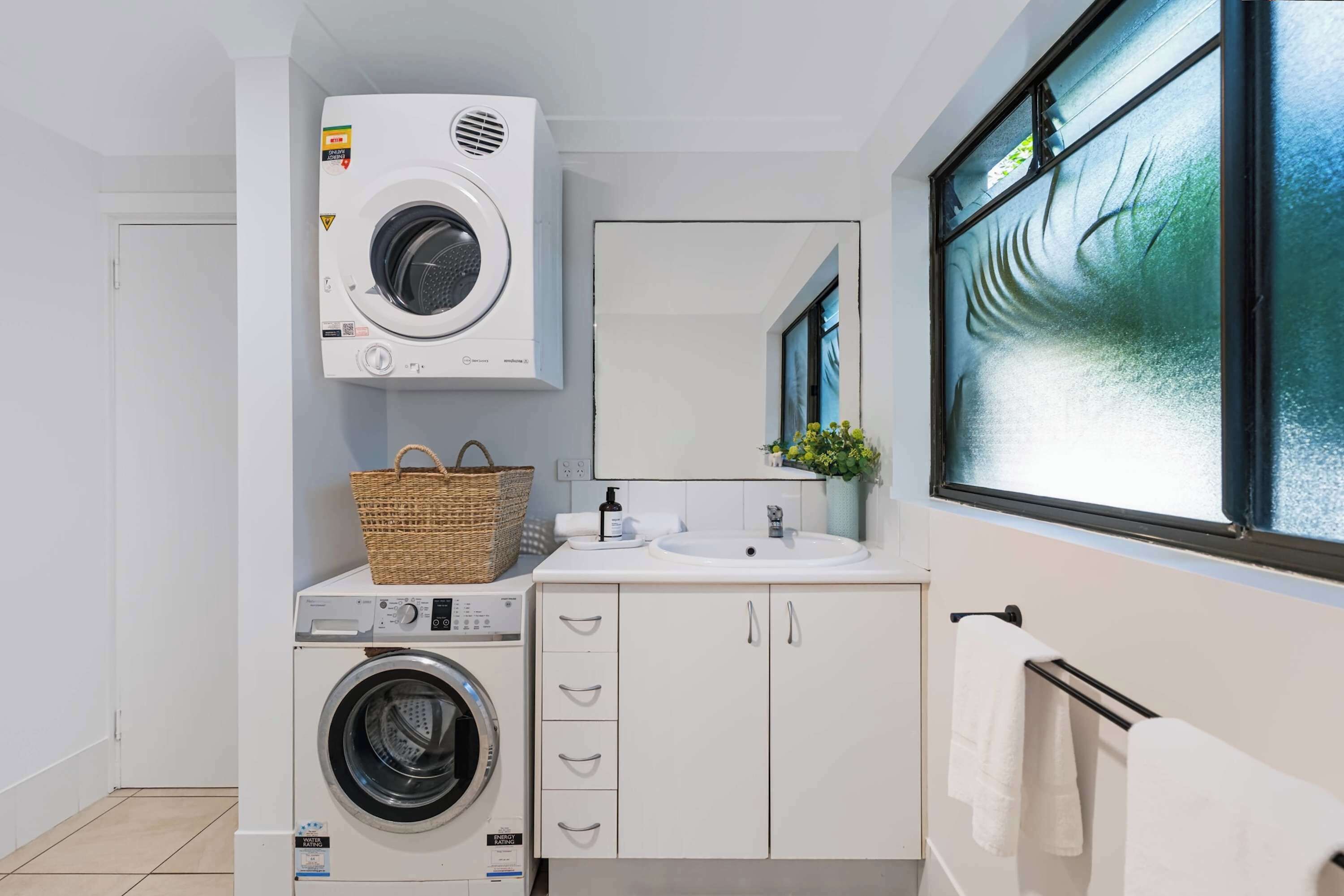 Een kleine wasruimte met een voorlader wasmachine, een droger en een wastafel met spiegel erboven.