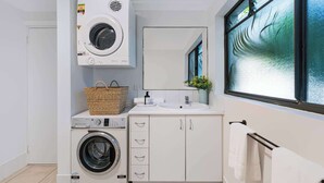 A compact laundry room with a front-loading washing machine, a dryer, and a sink with a mirror above it. - Chic Noosa Pad - Walk to Noosa Hastings St (Noosa)