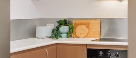 A kitchen with wooden cabinets, a white countertop, a toaster, a plant, and a cutting board.