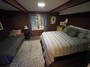 Un dormitorio con cama, mesita de noche, lámpara, ventana con cortinas y alfombra.