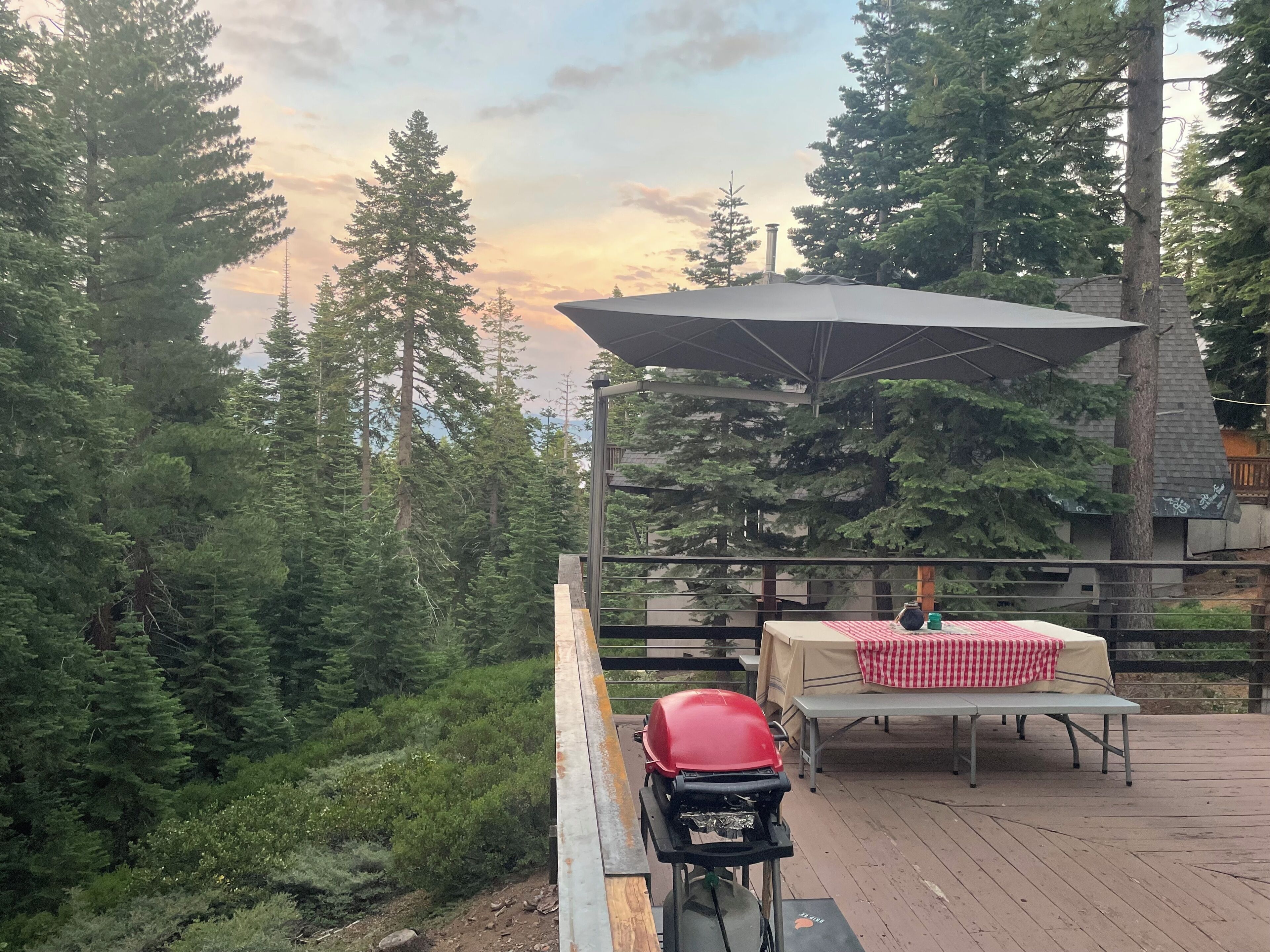 Una terrazza con una griglia barbecue, un tavolo con tovaglia a quadri e un ombrellone grande.