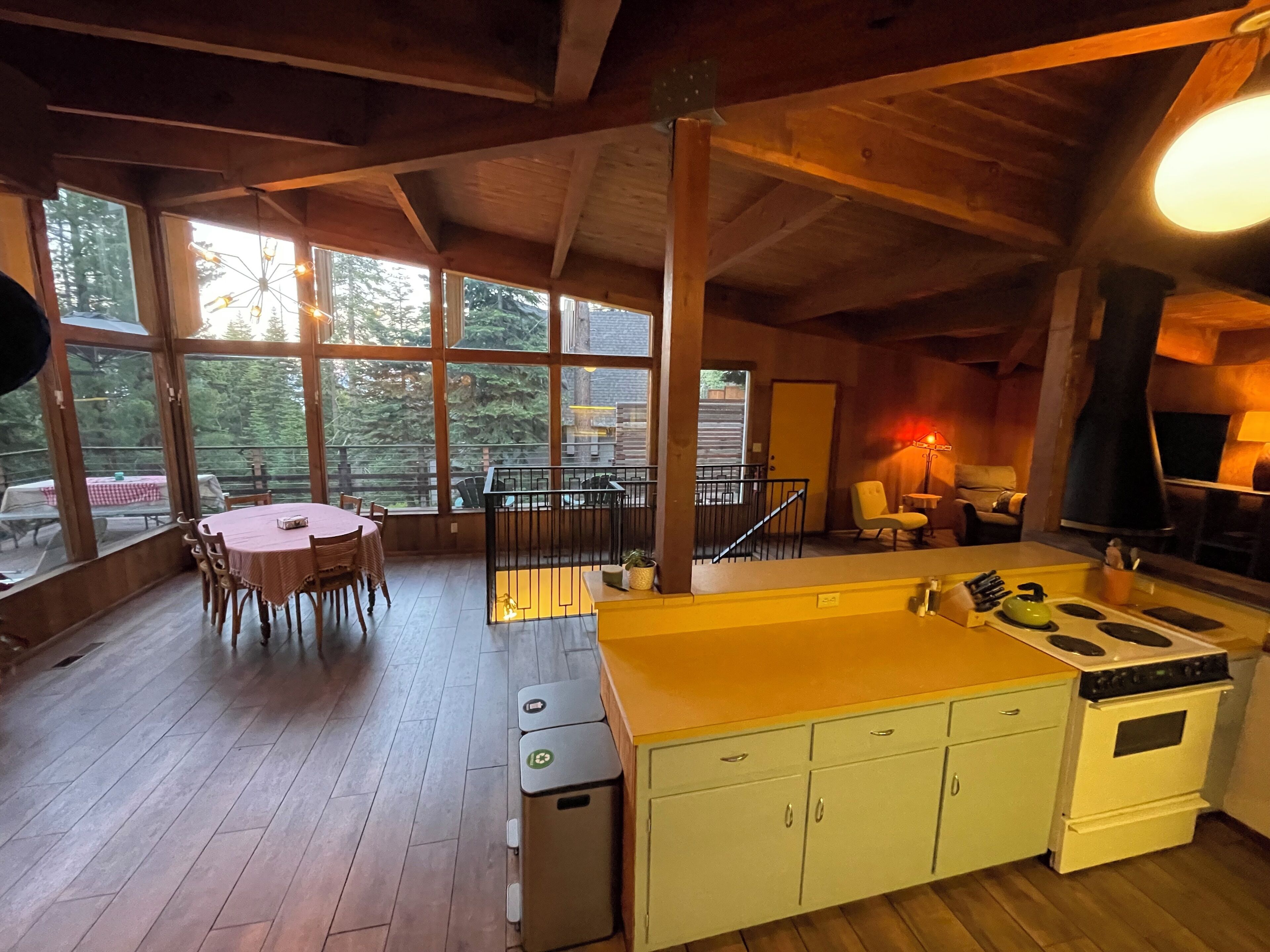 A kitchen with a central island, a dining area with a table and chairs, and large windows offering a view of the outdoors.