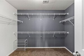 Ein Zimmer mit grauer Wand, weißer Decke und braunem Teppich. An der Wand sind zwei weiße Metallregale angebracht.