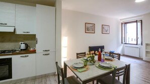 A modern kitchen with white cabinets, a stove, and a kettle. There is a dining area with a table set for two, plates, and a vase of flowers. - Cozy apartment in Carro with WiFi (Carro)